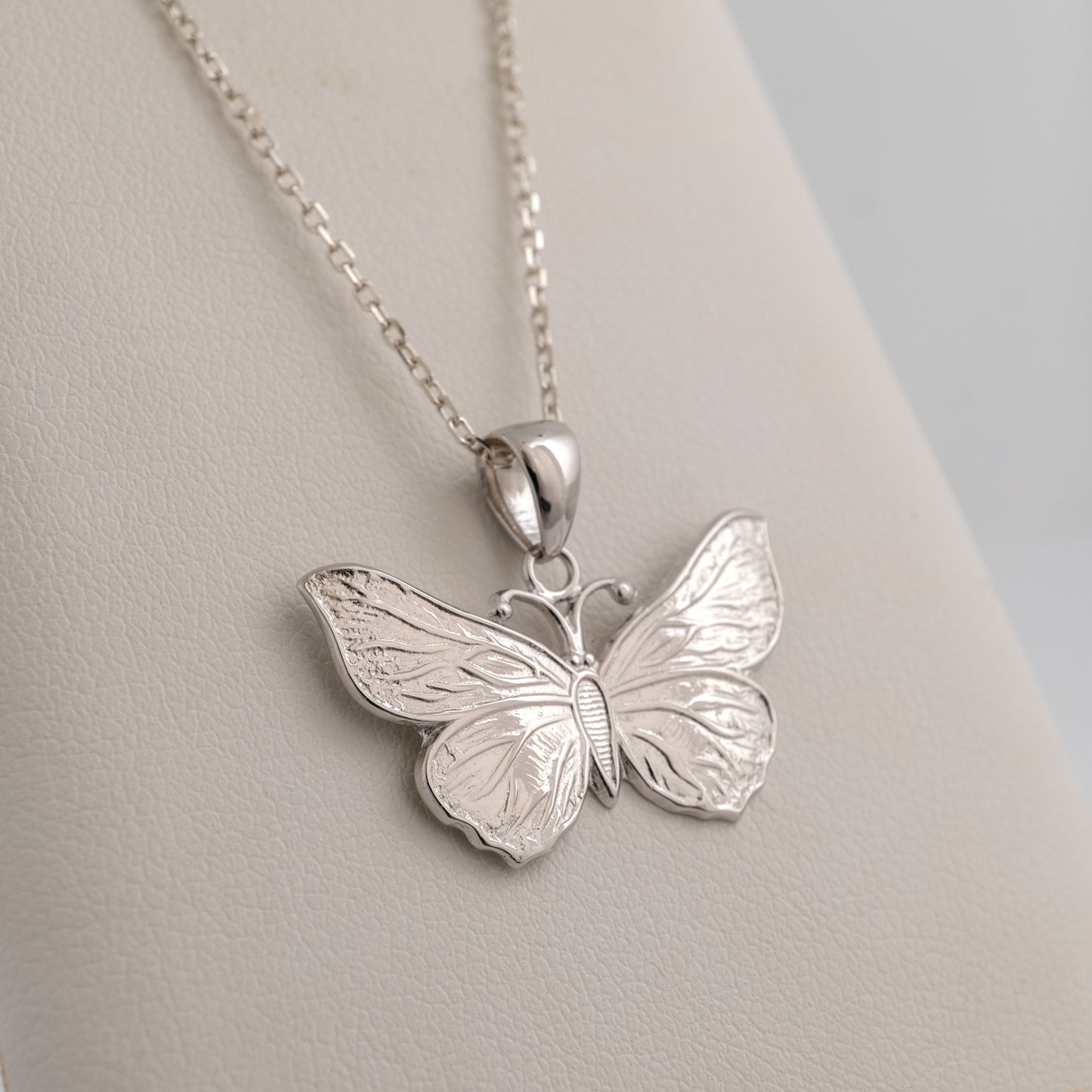 Silver butterfly pendant on a chain against a light gray background