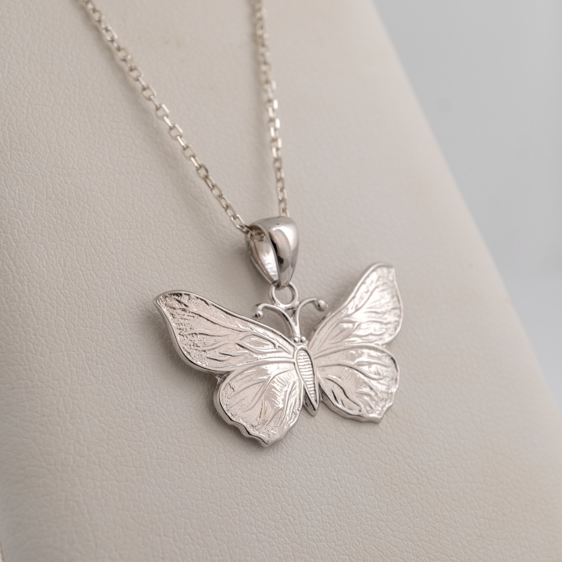 Silver butterfly pendant on a chain against a light gray background