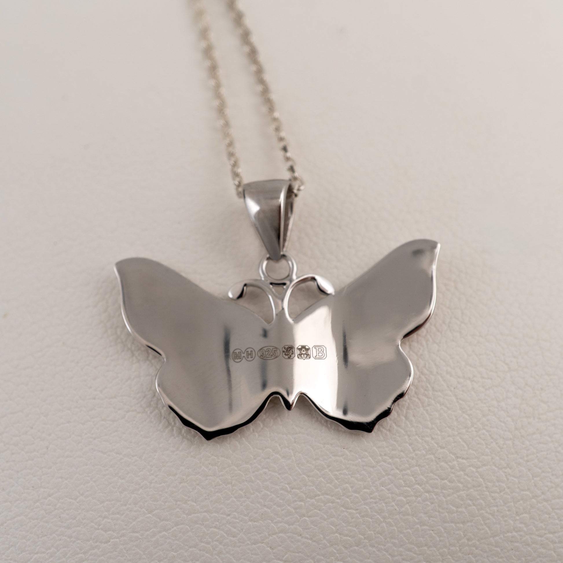 Silver butterfly pendant reverse side showing hallmarks on a chain against a light background