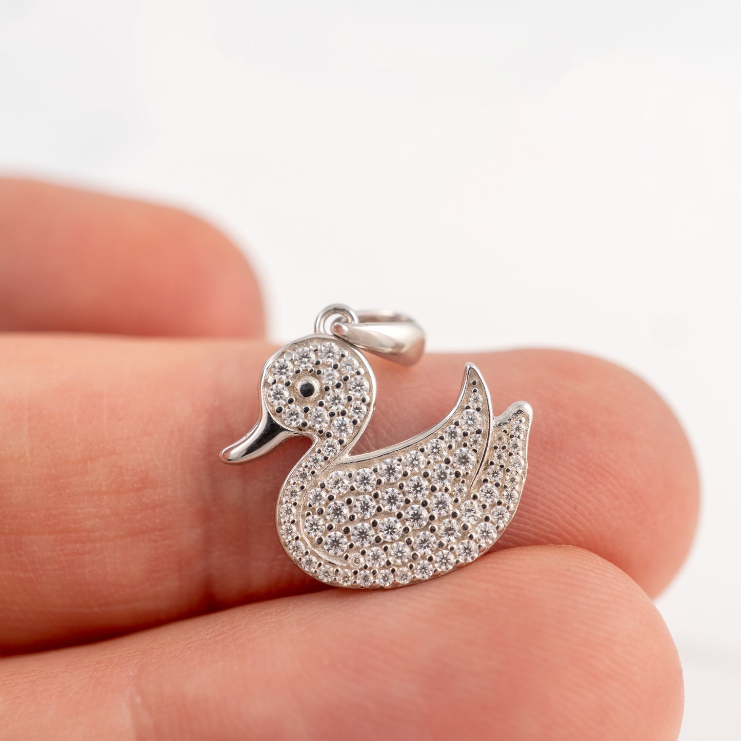 Silver duck-shaped pendant with gemstones held between fingers on a white background