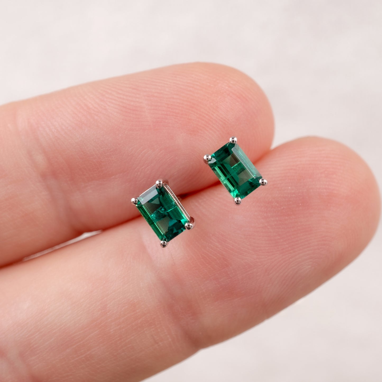 zambian green emerald stud earrings held between two fingers on a light background