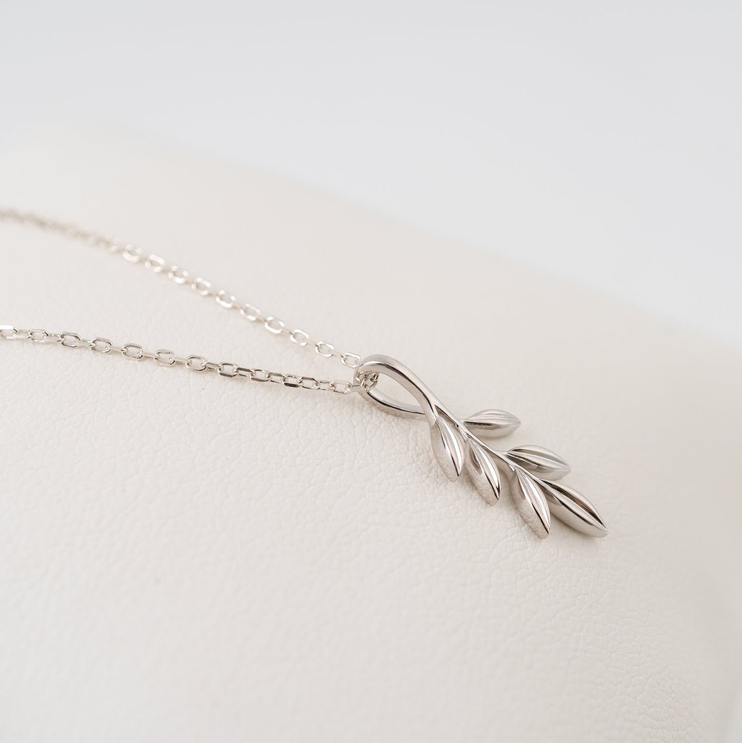 Silver olive branch necklace on a light gray background