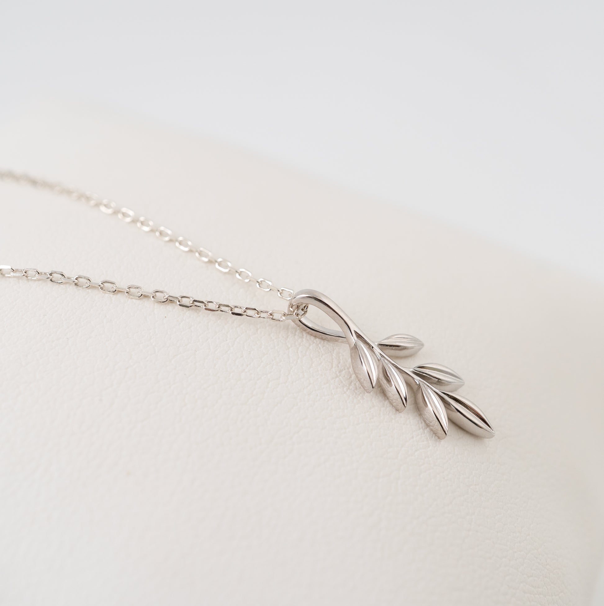 Silver olive branch necklace on a light gray background