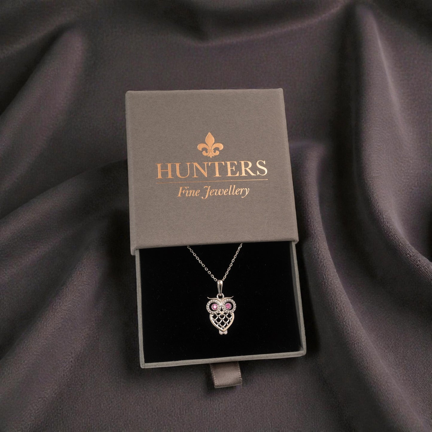 silver Owl-shaped necklace in a Hunters Fine Jewellery box on a dark fabric background