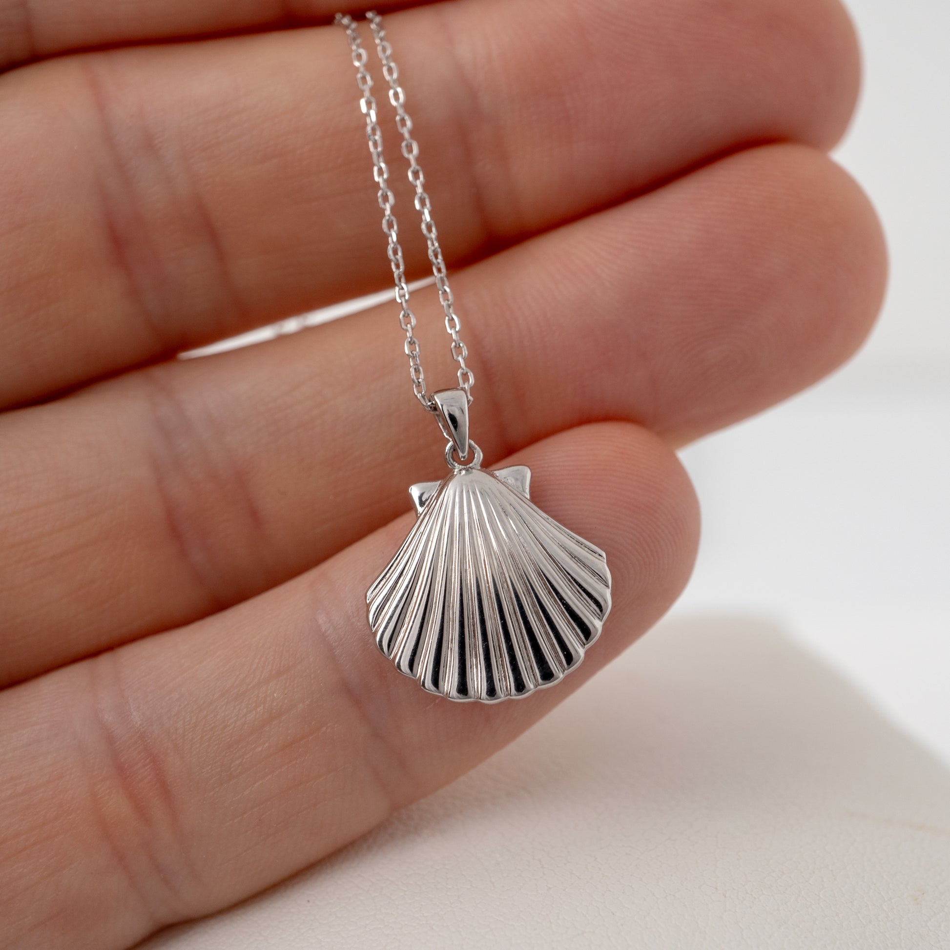 silver scallop shell necklace in sterling silver in a hand showing scale