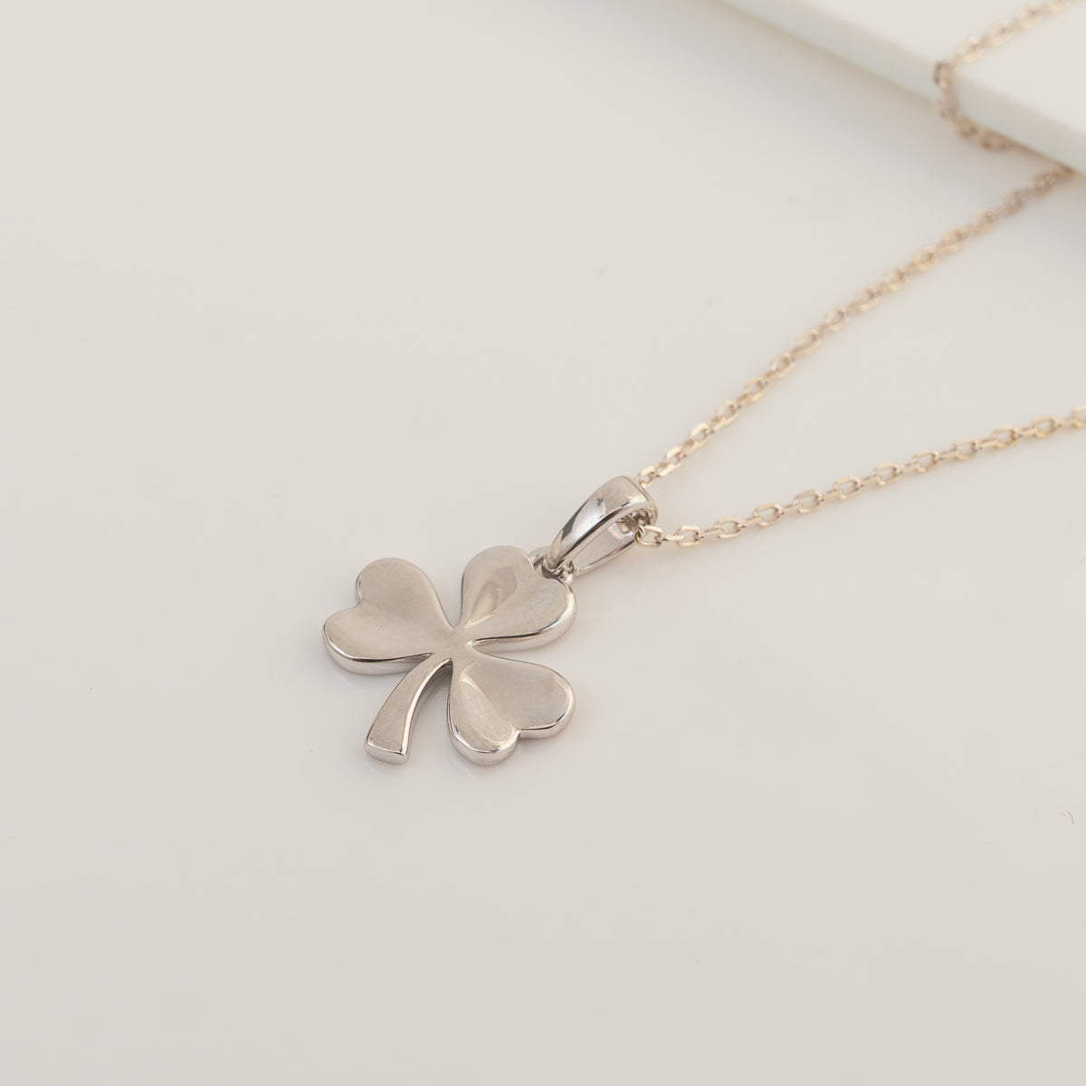 A silver three-leaf clover shamrock pendant necklace on a delicate gold-tone chain, displayed on a clean white background.