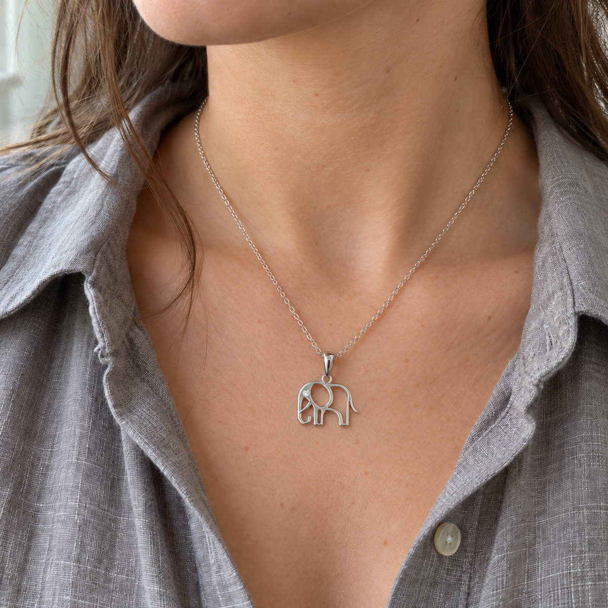 silver elephant necklace on a womans neck with open grey shirt