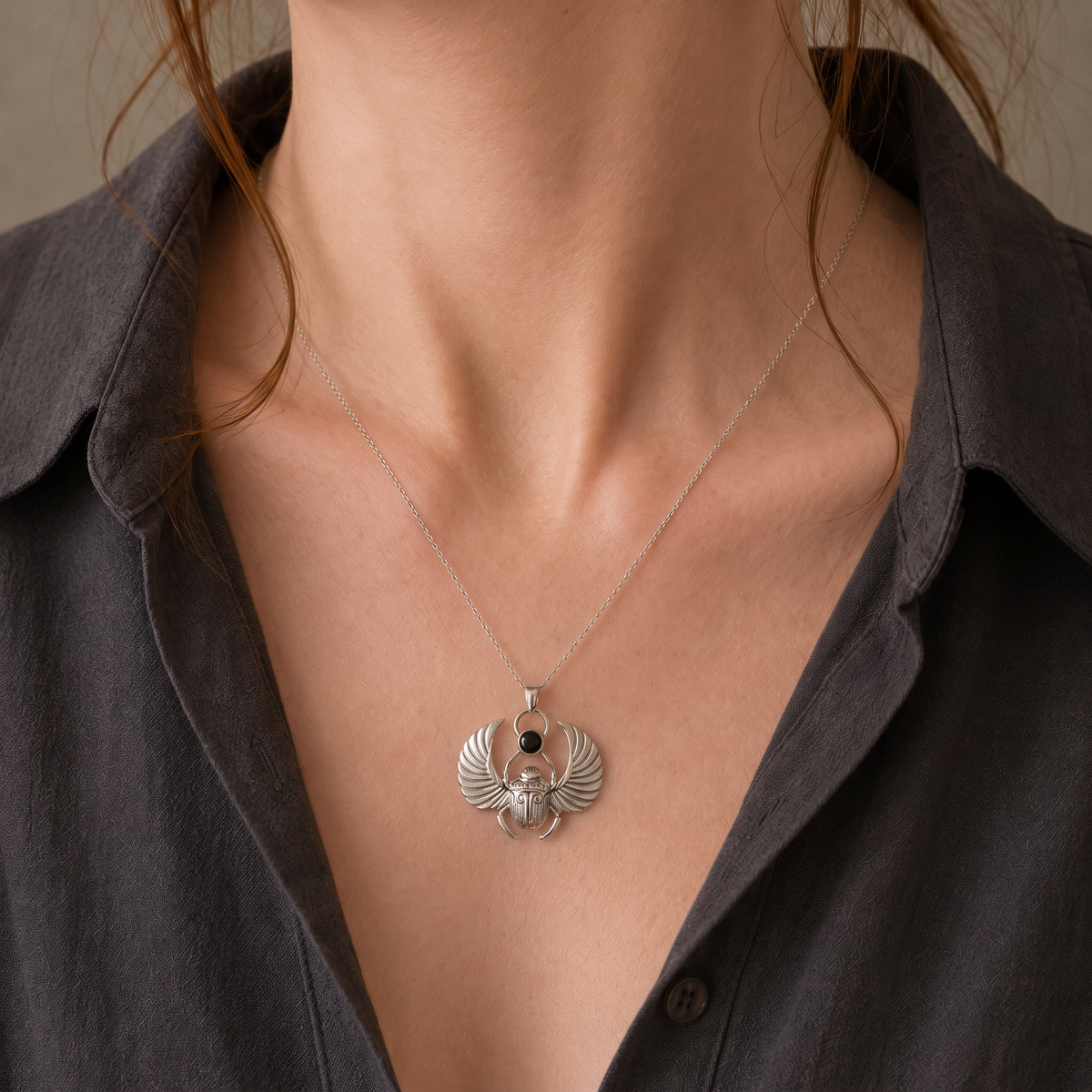 Silver scarab pendant with polished black onyx worn by a female model in a dark open shirt, showing the pendant’s scale.