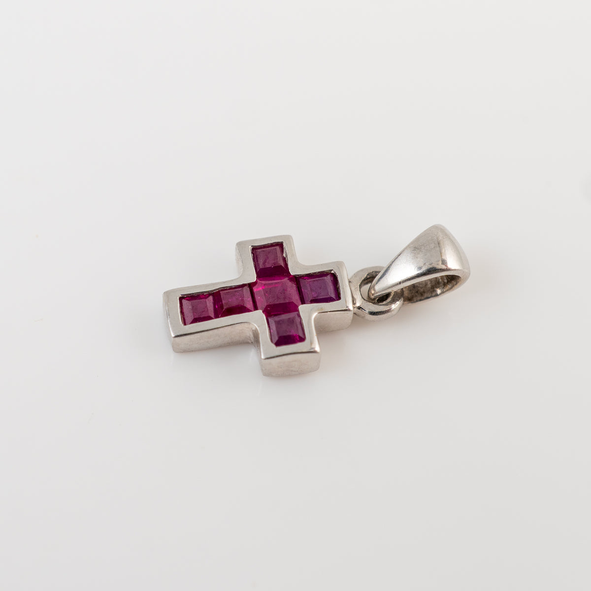 A white gold cross pendant featuring a central five-stone ruby cluster, photographed on a clean white background.