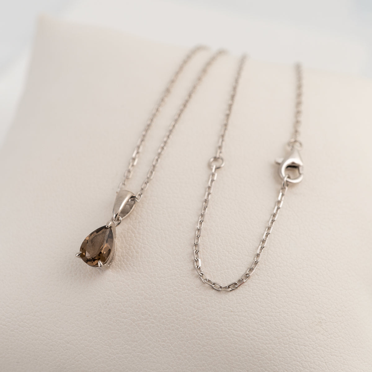 Smoky quartz teardrop necklace in sterling silver draped over a white cushion, showing the adjustable chain.