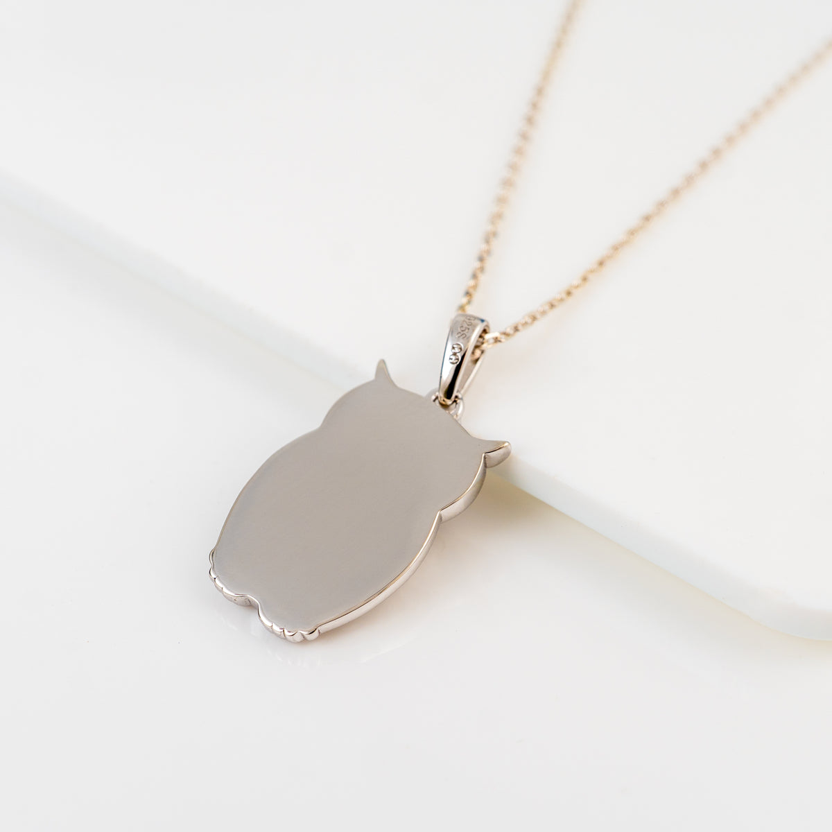 A plain silver owl-shaped pendant necklace on a delicate gold-tone chain, displayed on a clean white surface.