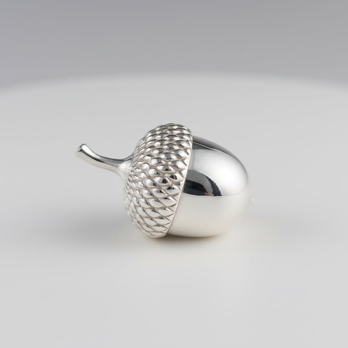 miniature Silver acorn-ornament figurine on a light gray background