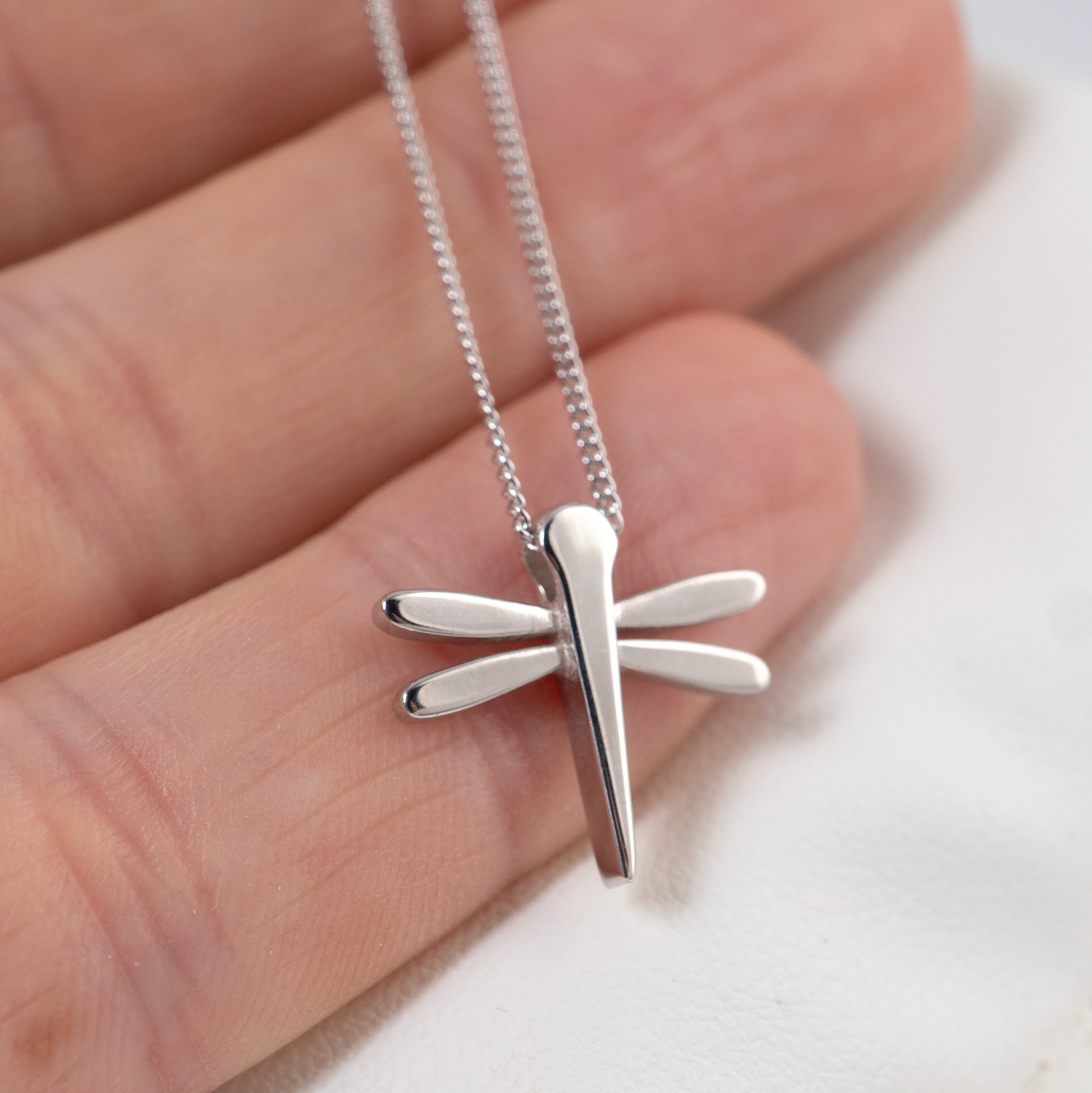 Silver dragonfly pendant on a chain held between fingers