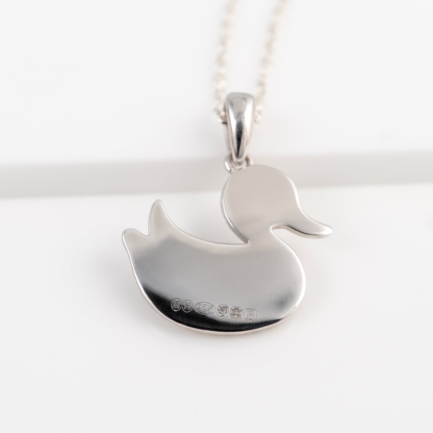 Silver duck-shaped pendant reverse side assay hallmarks on a white background