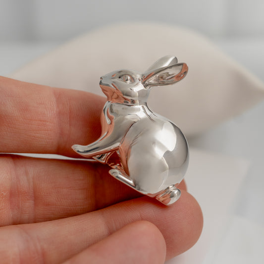 Silver rabbit-shaped object held in a hand against a neutral background