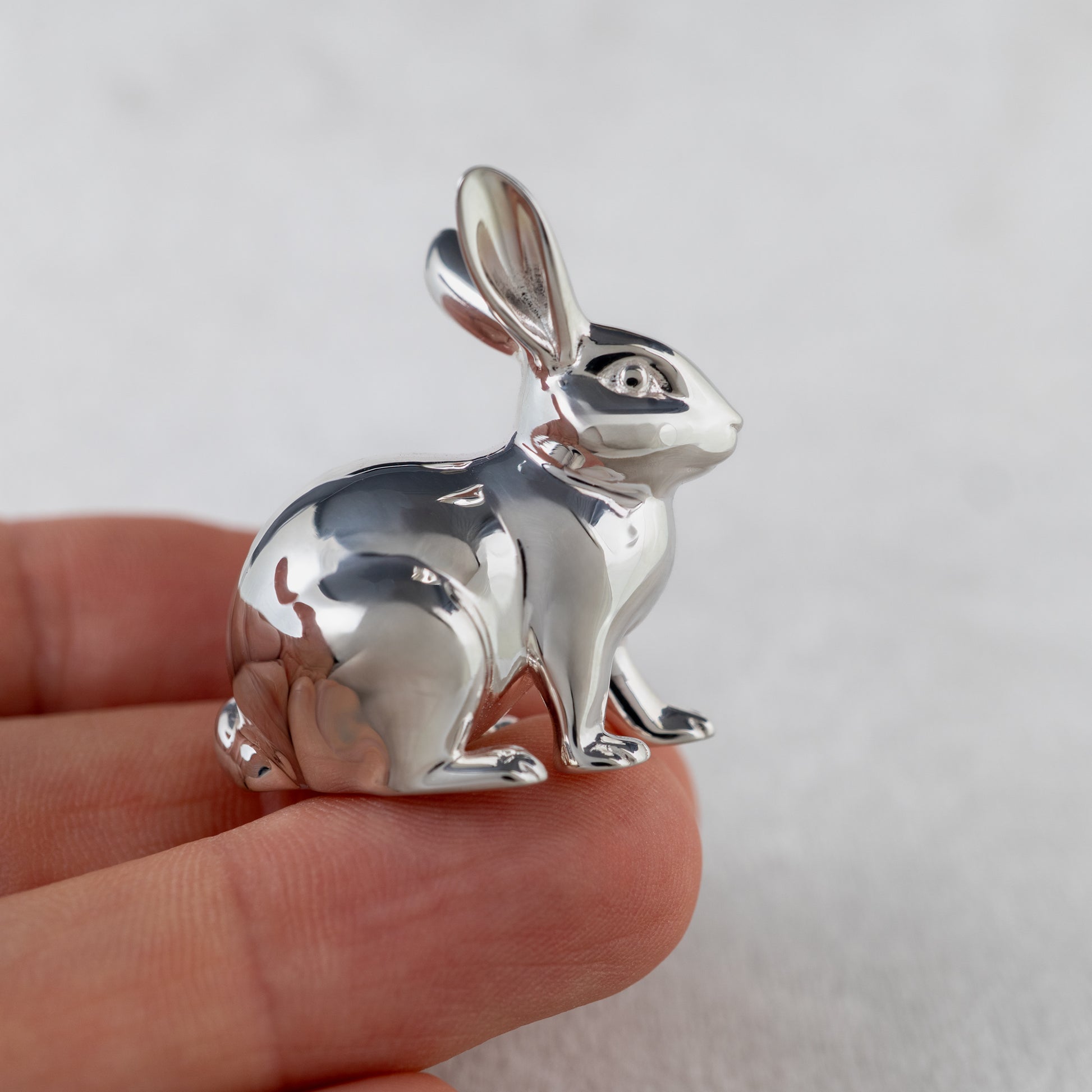 Silver rabbit pendant held in a hand against a plain background