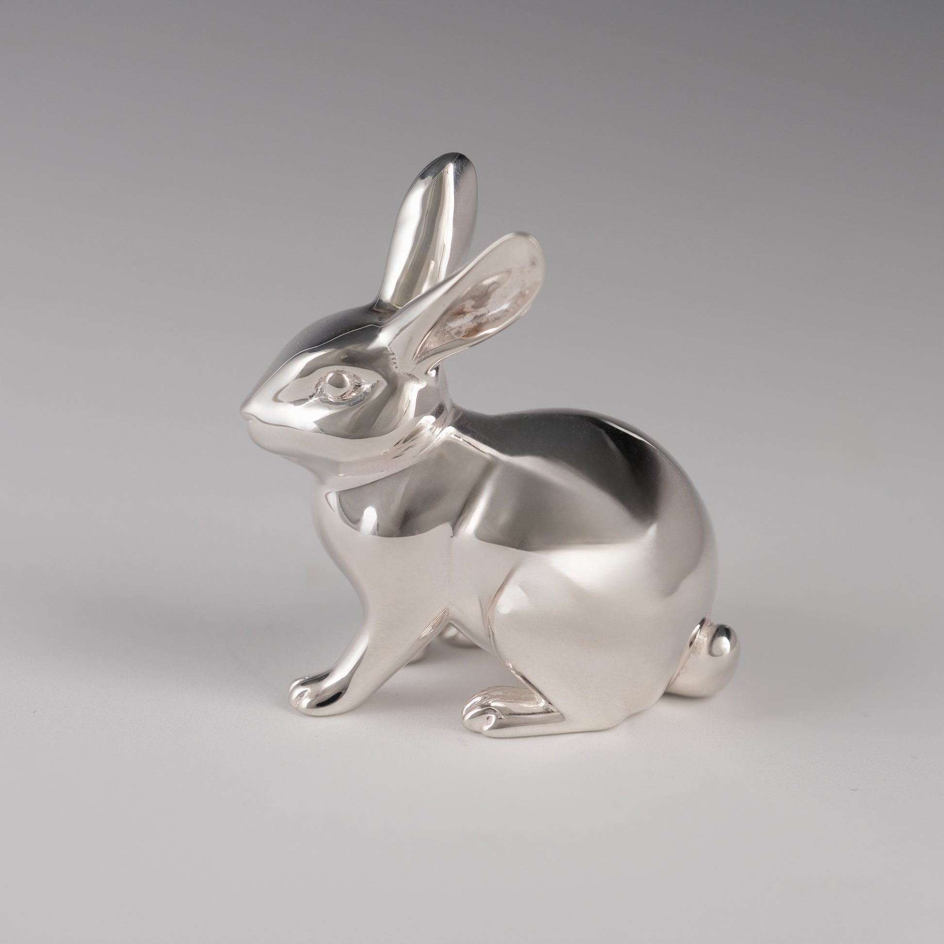 Silver rabbit figurine side view on a gray background