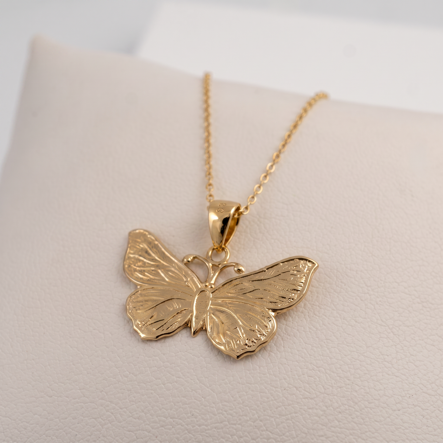 A gold butterfly pendant necklace displayed on a soft cream-colored jewelry cushion.