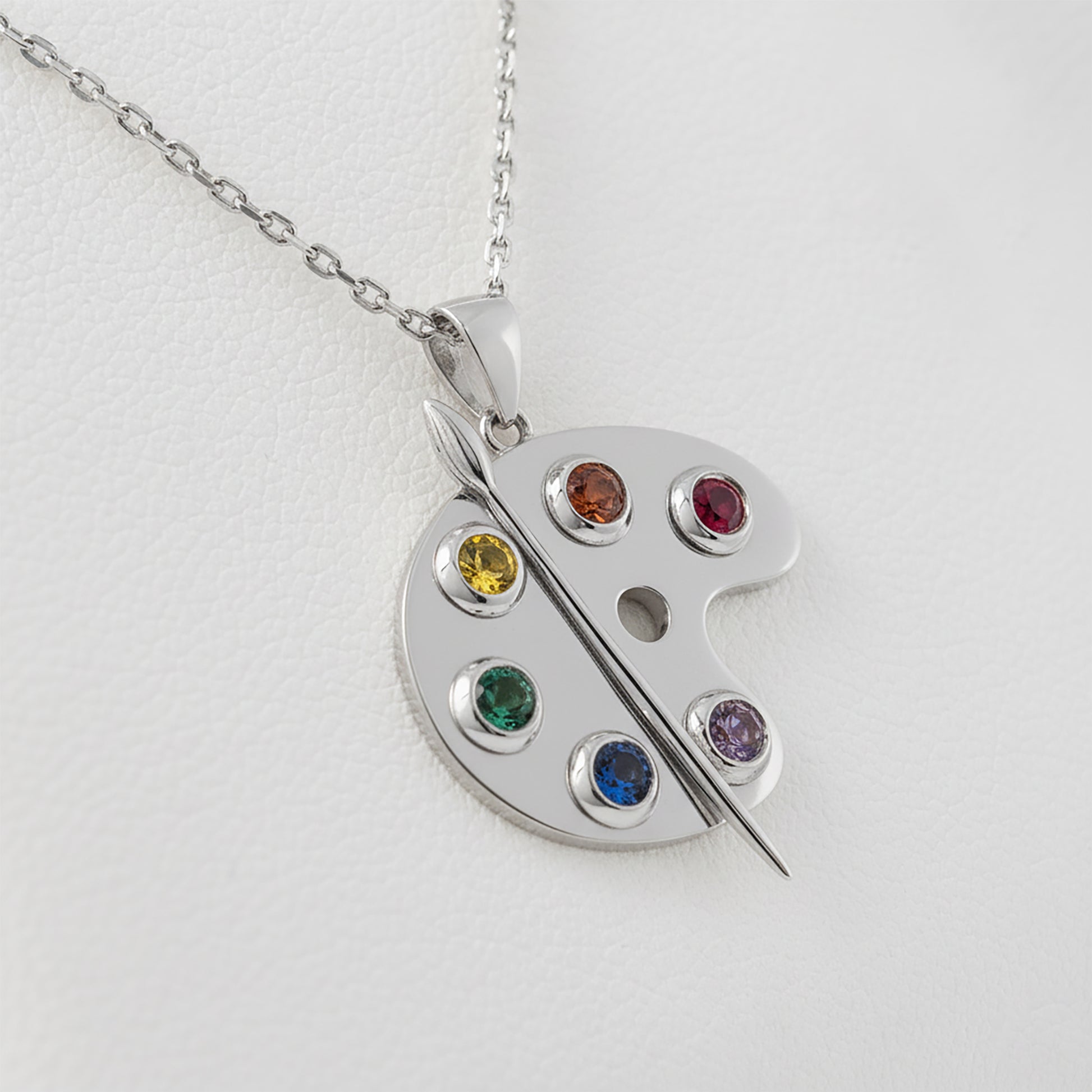 Silver artist paint palette pendant featuring colorful gemstones on a light gray background