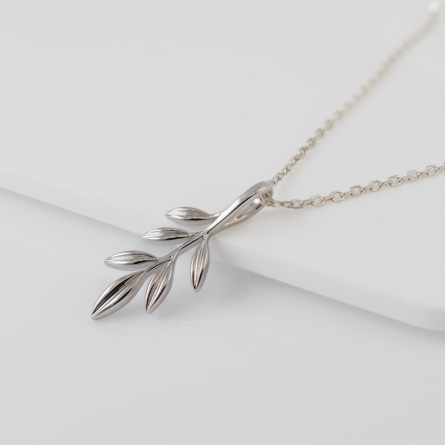 Silver olive branch necklace on a white surface
