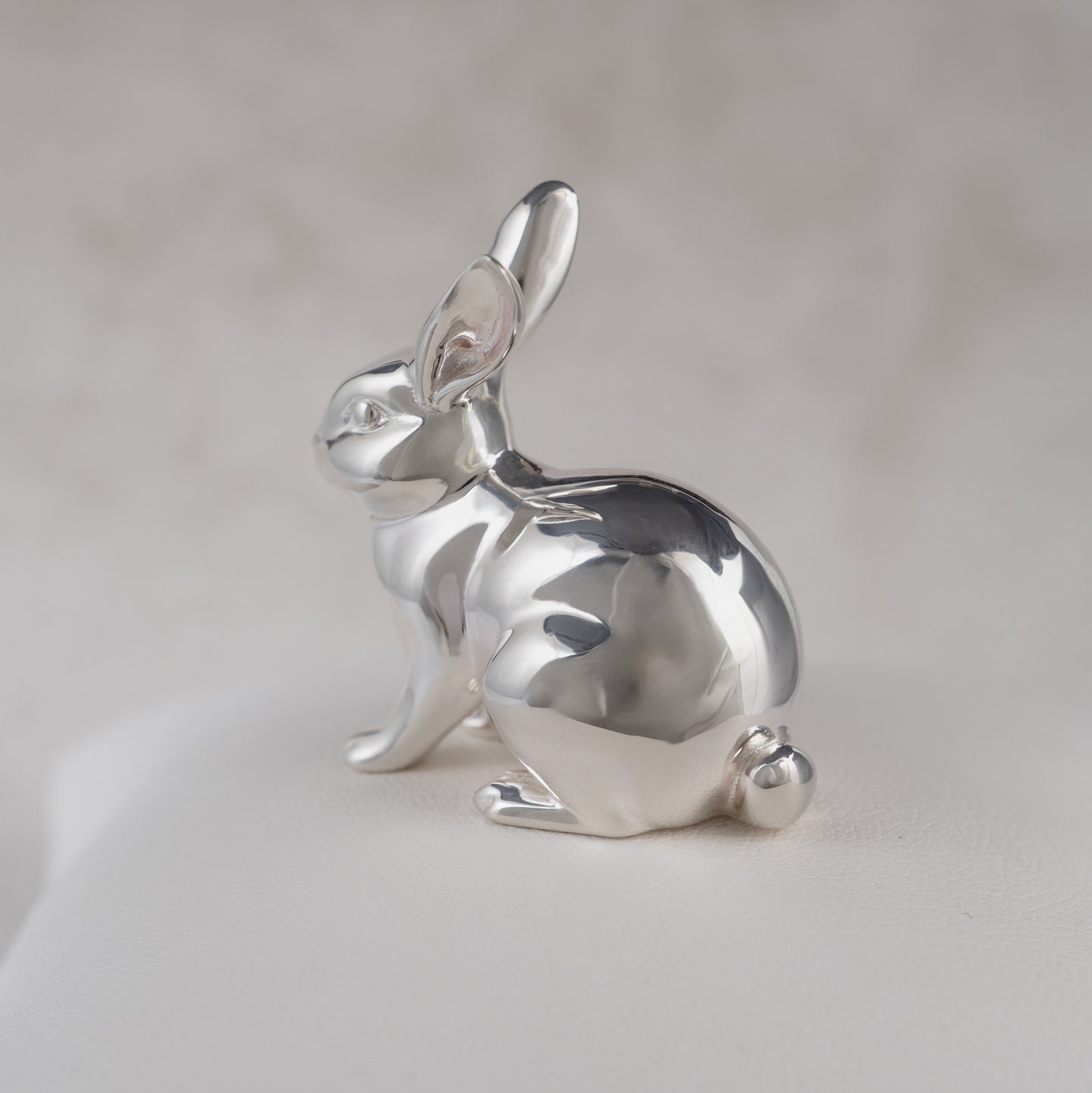 Silver rabbit figurine slight angle on a light gray background