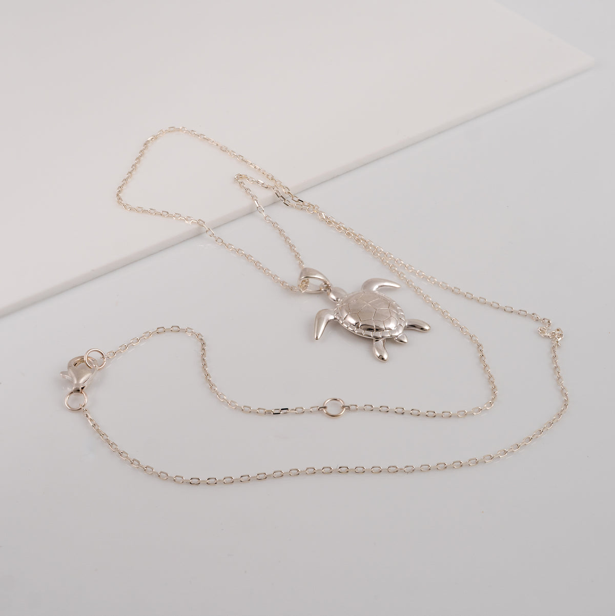 Sterling silver sea turtle necklace laid flat, showing the cable chain, lobster clasp and adjustment rings
