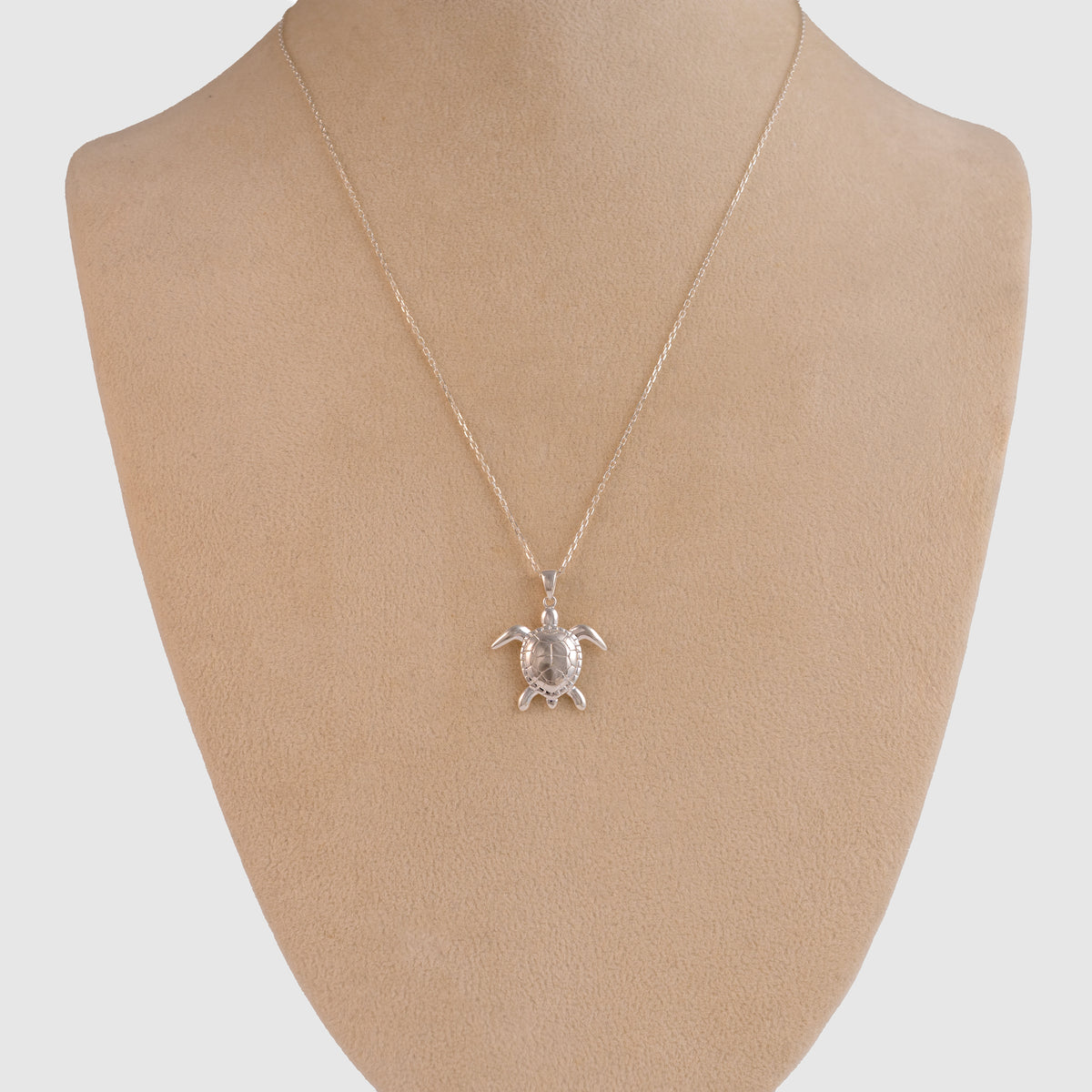 Sterling silver sea turtle necklace hanging on a beige jewellery display bust