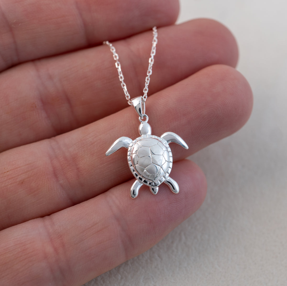 Sterling silver sea turtle pendant resting against fingers, showing its size and detailed shell