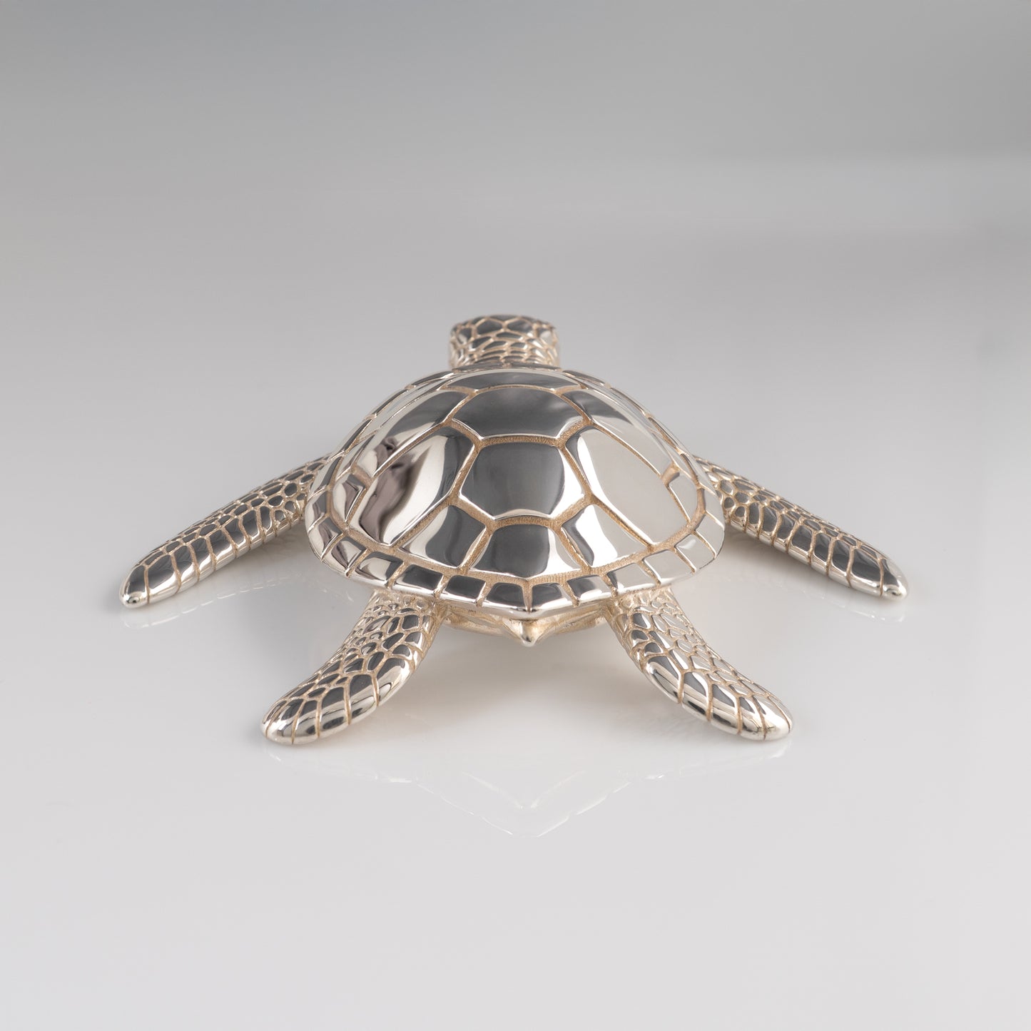 Silver sea turtle figurine back view on a light gray background