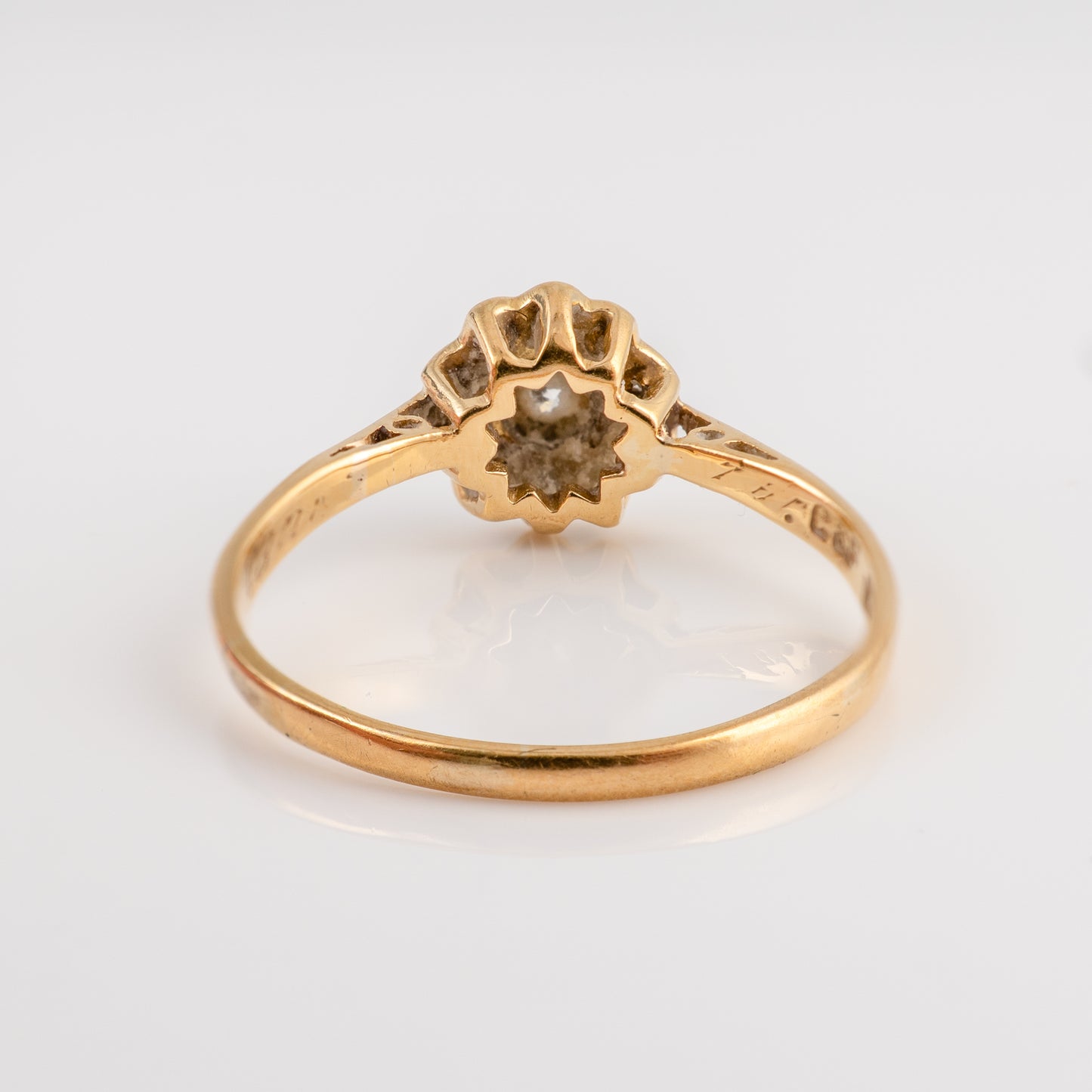 A vintage yellow gold ring with a flower-shaped setting and a small central gemstone, shown on a plain light gray background.