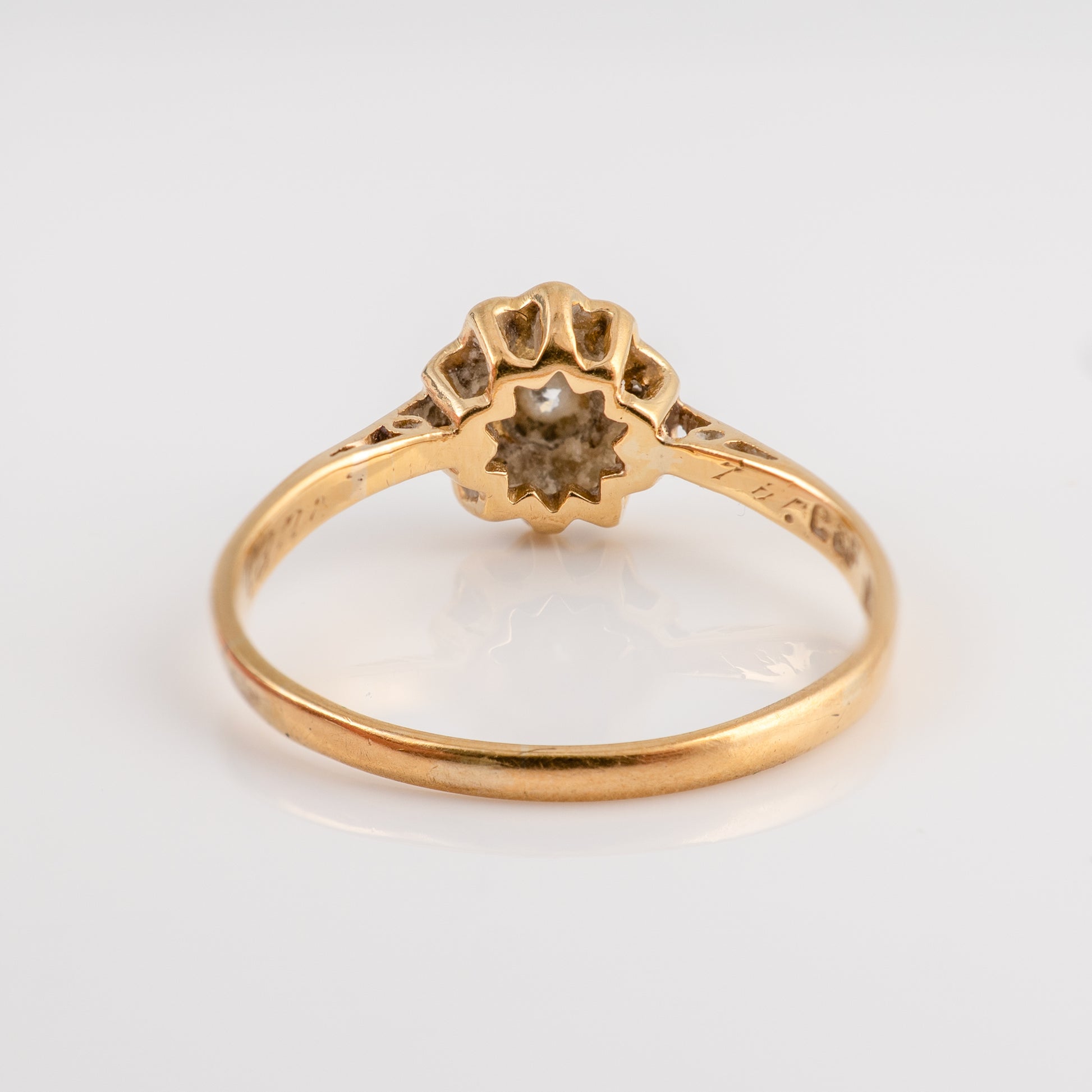 A vintage yellow gold ring with a flower-shaped setting and a small central gemstone, shown on a plain light gray background.