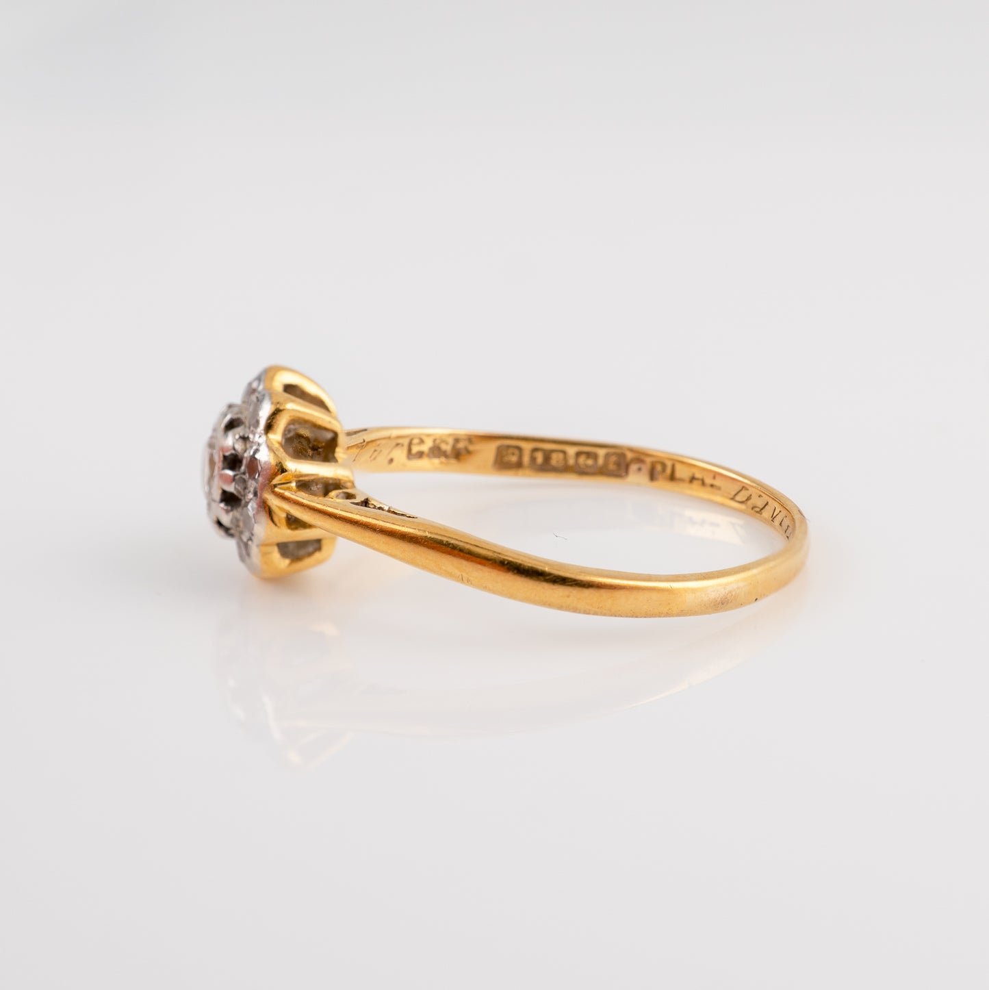 A yellow gold diamond ring with a small cluster of clear gemstones in a prong setting, photographed on a clean white reflective surface. The inside of the band is engraved Birmingham assay hallmarks
