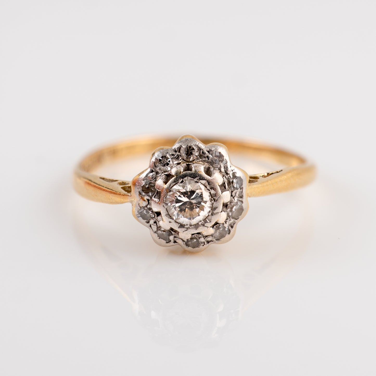 A vintage diamond cluster ring featuring a central round diamond surrounded by a halo of small diamonds, set on a yellow gold band with silver-colored accents, photographed on a clean white background.