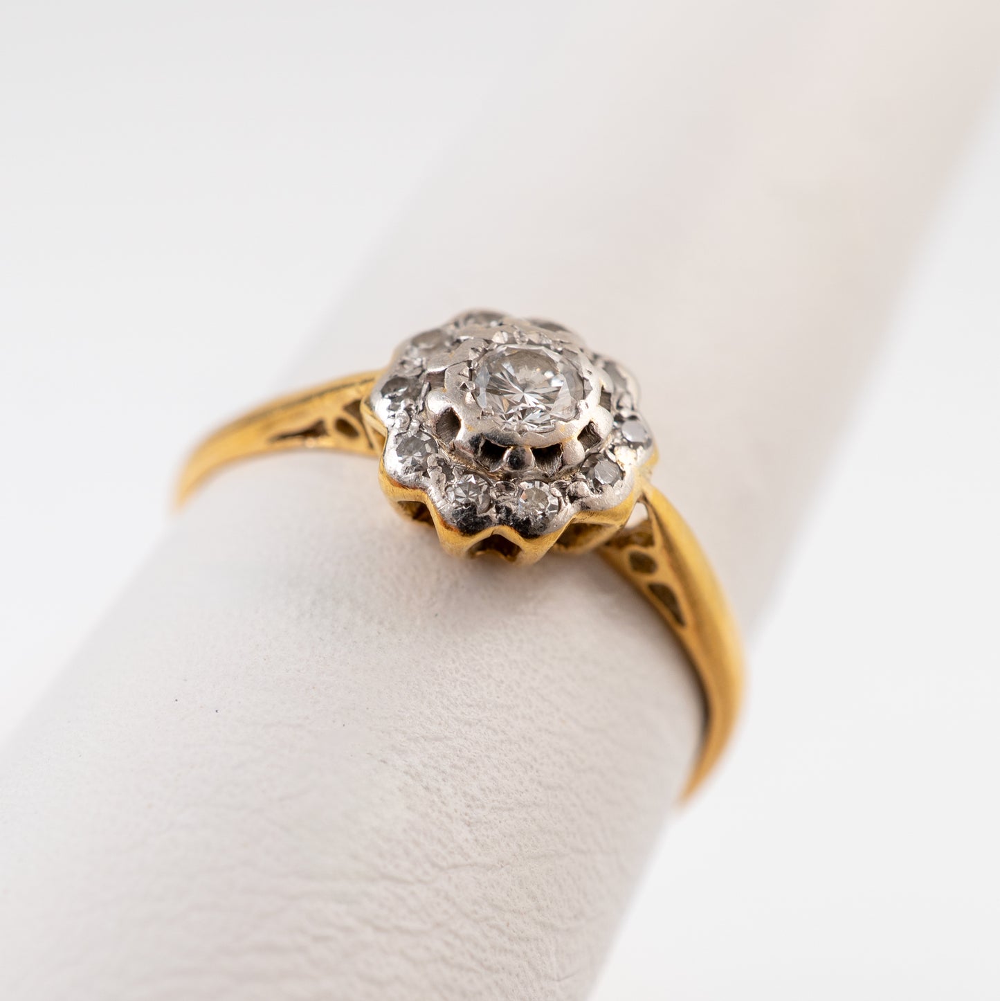 A vintage diamond ring with a yellow gold band and a silver-toned floral cluster setting featuring a central clear gemstone, displayed on a white ring stand.