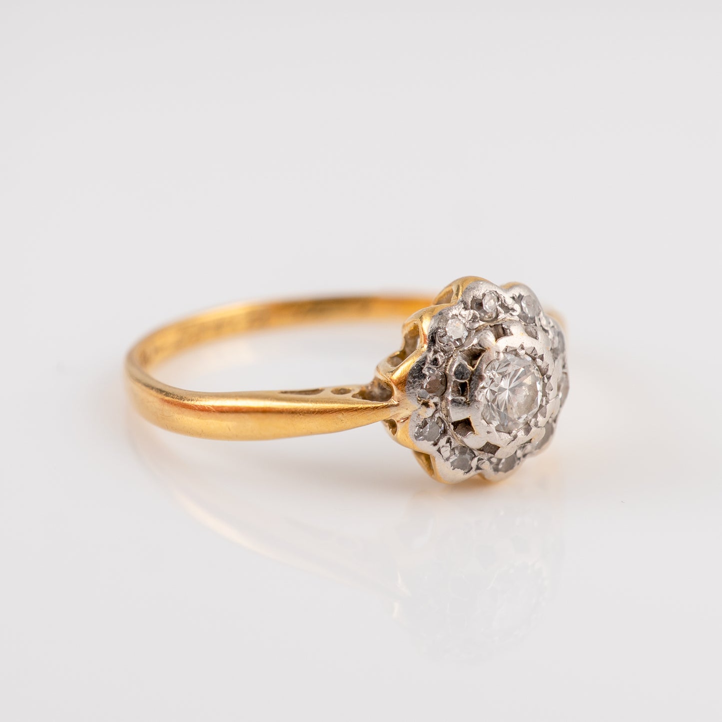A vintage diamond ring featuring a yellow gold band and a cluster setting with a central round diamond surrounded by smaller diamonds, set against a clean white background.