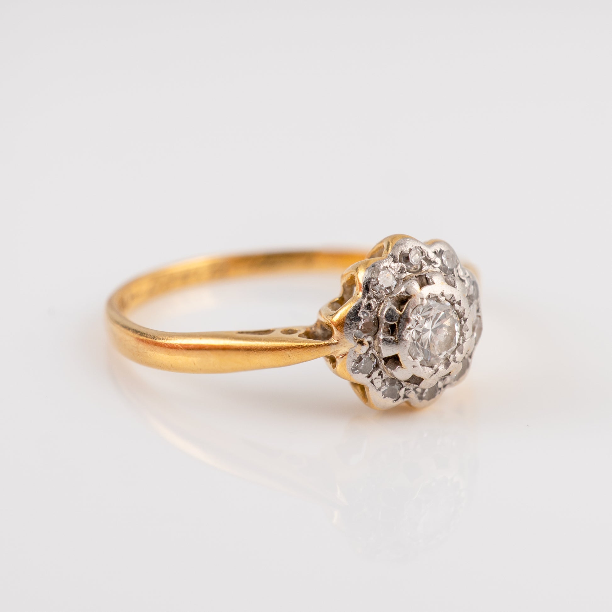 A vintage diamond ring featuring a yellow gold band and a cluster setting with a central round diamond surrounded by smaller diamonds, set against a clean white background.
