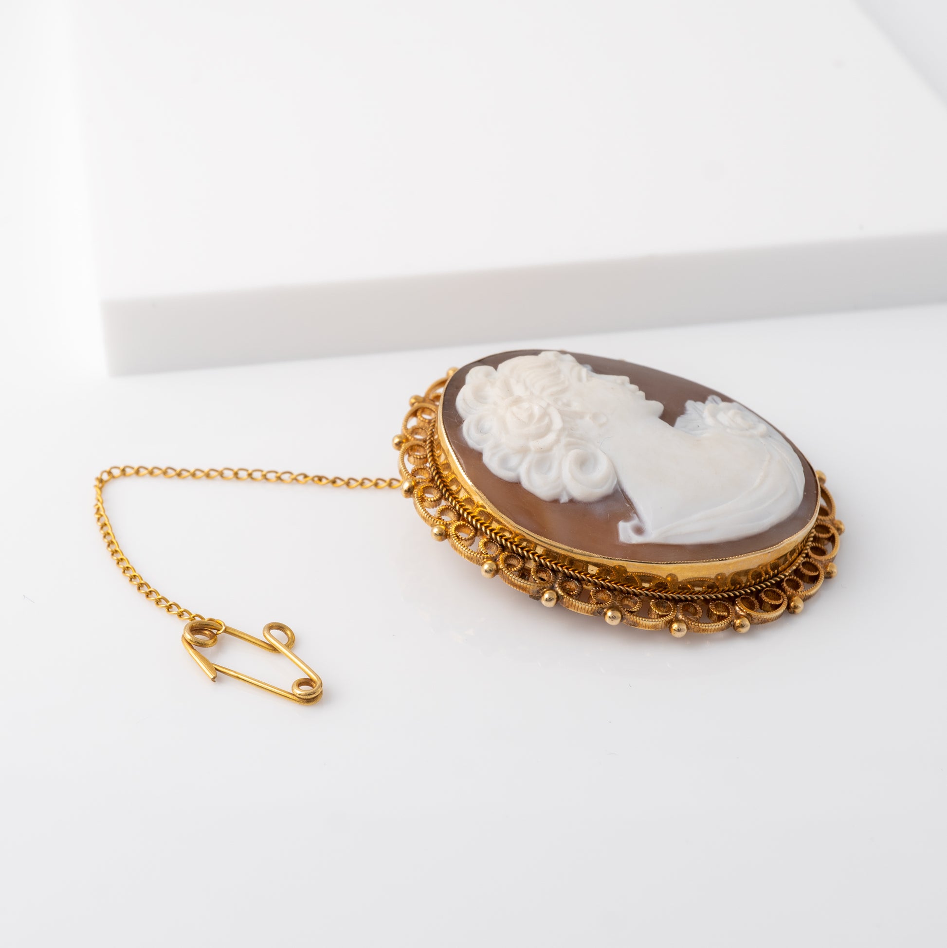 Side view of vintage cameo brooch with rope and ball border details with safety chain