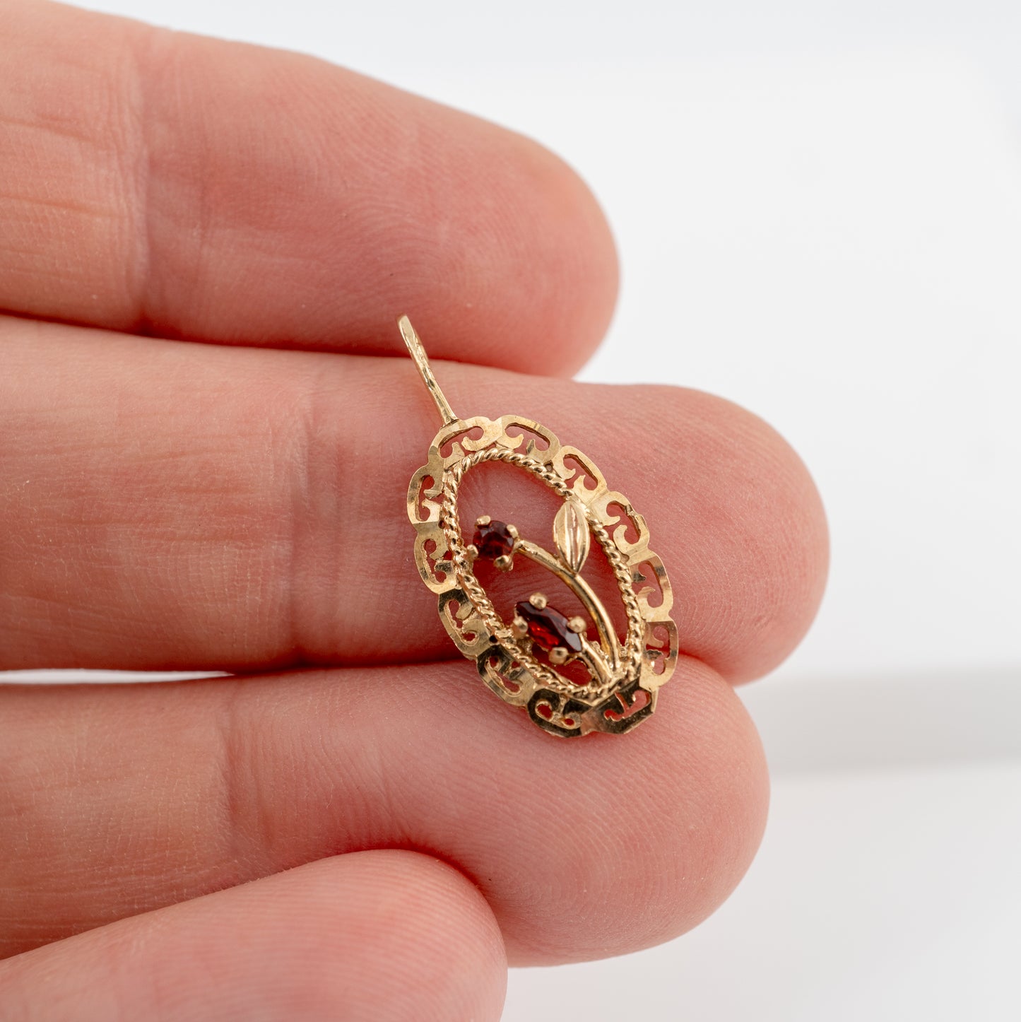 A gold filigree pendant with small garnet gemstones, held between fingers to show its small scale.