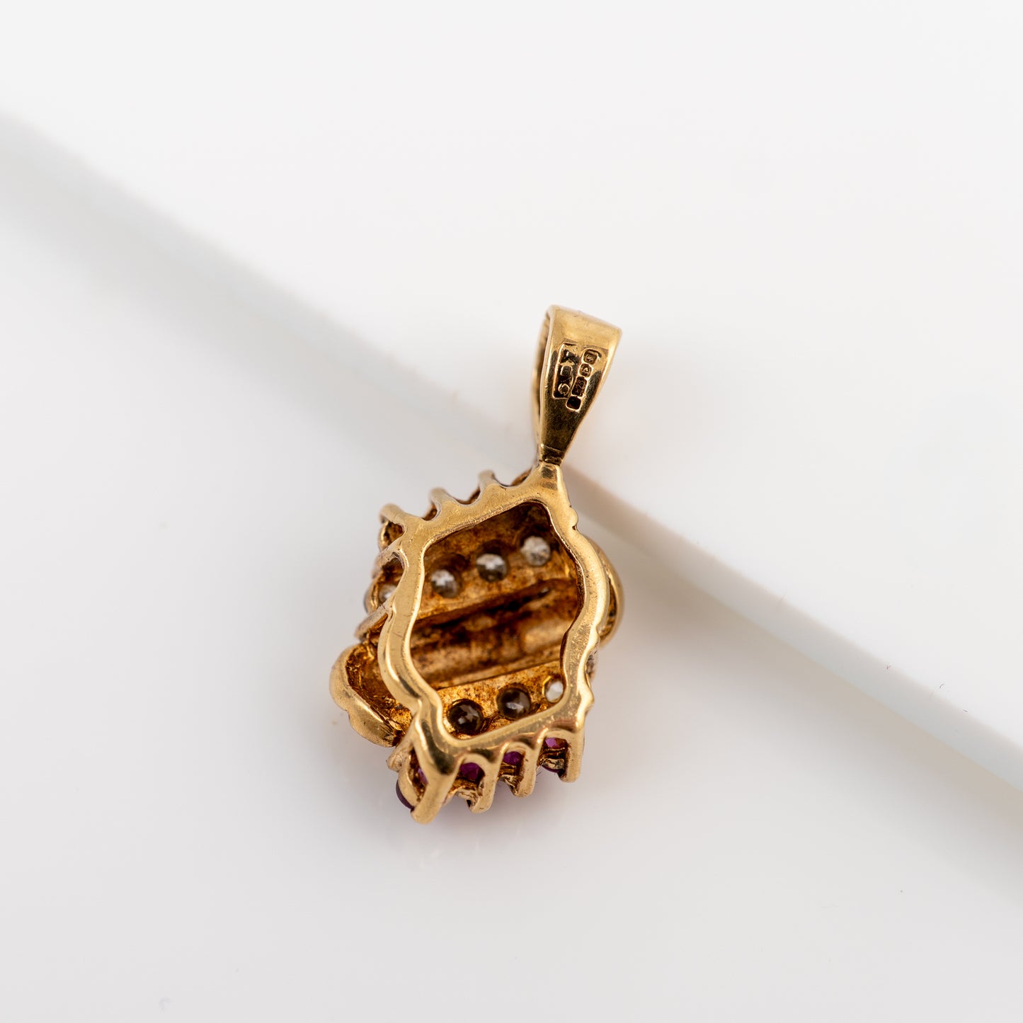 A gold pendant featuring a textured, organic shell-like design with small dark brown and clear gemstone accents, displayed on a clean white background.