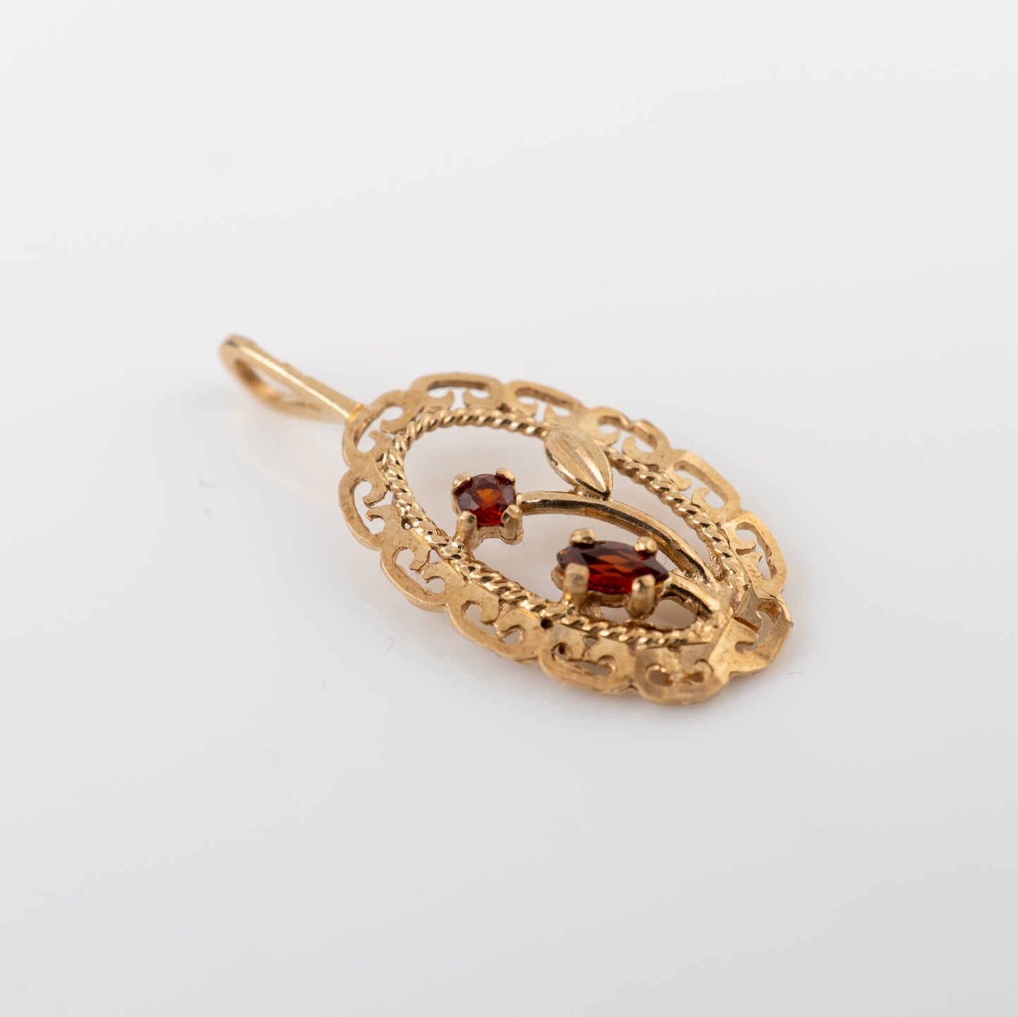 A vintage gold filigree pendant featuring two small oval-cut red gemstones, displayed on a clean white background.