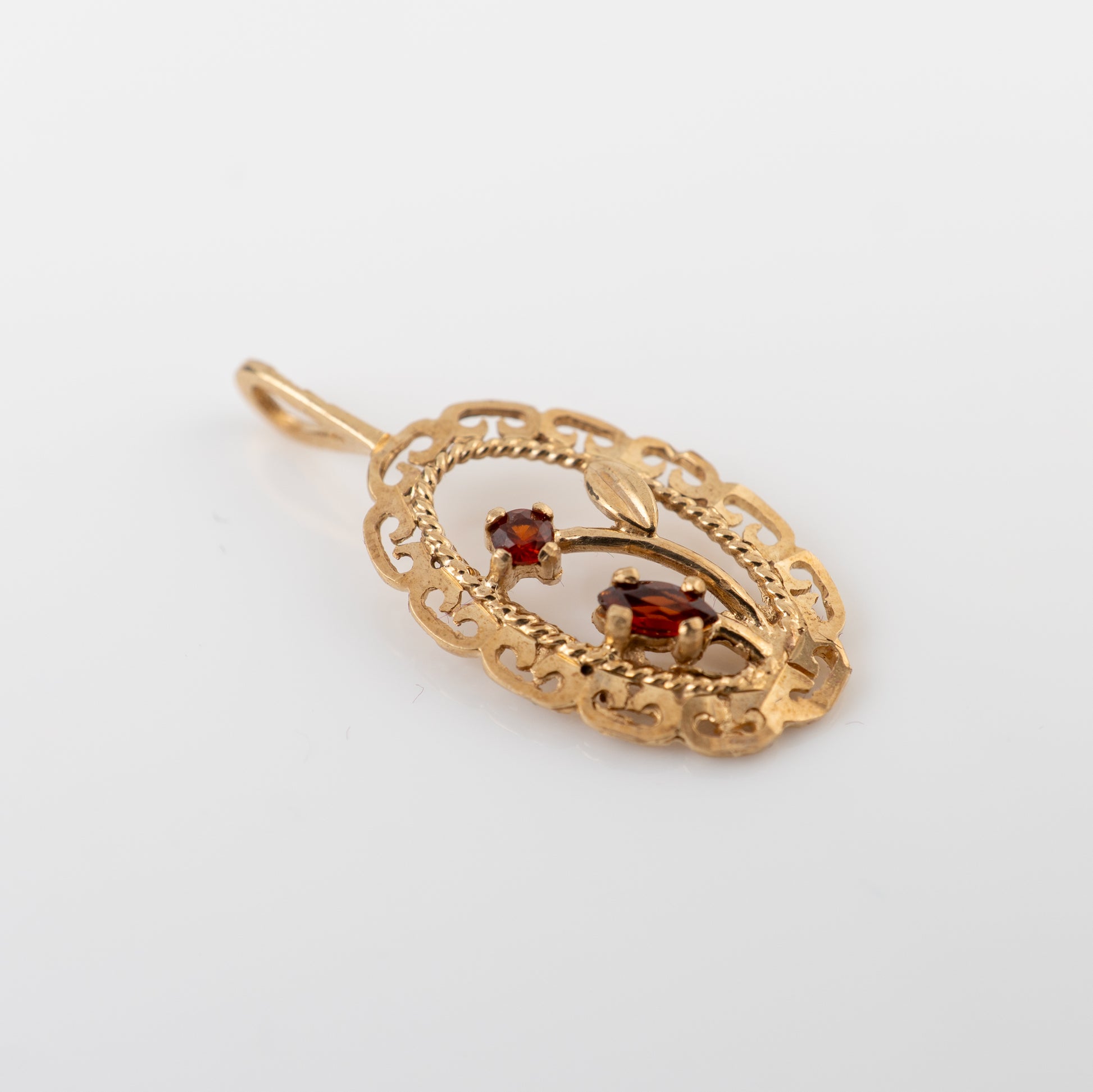 A vintage gold filigree pendant featuring two small oval-cut red gemstones, displayed on a clean white background.