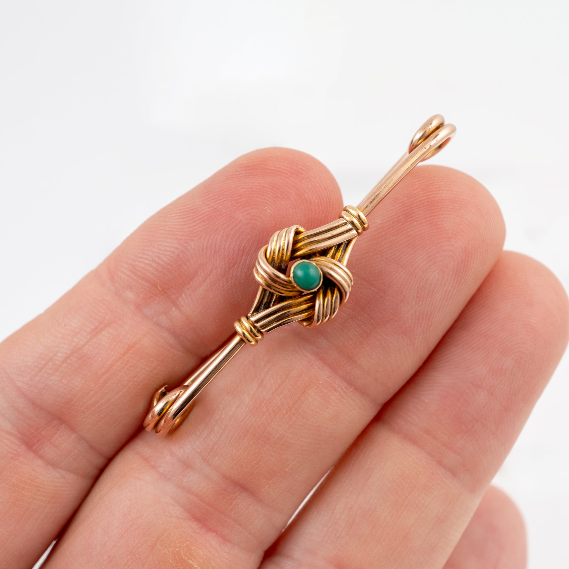 A small gold brooch with a central green turquoise cabochon stone, held on a person's fingers against a plain white background.