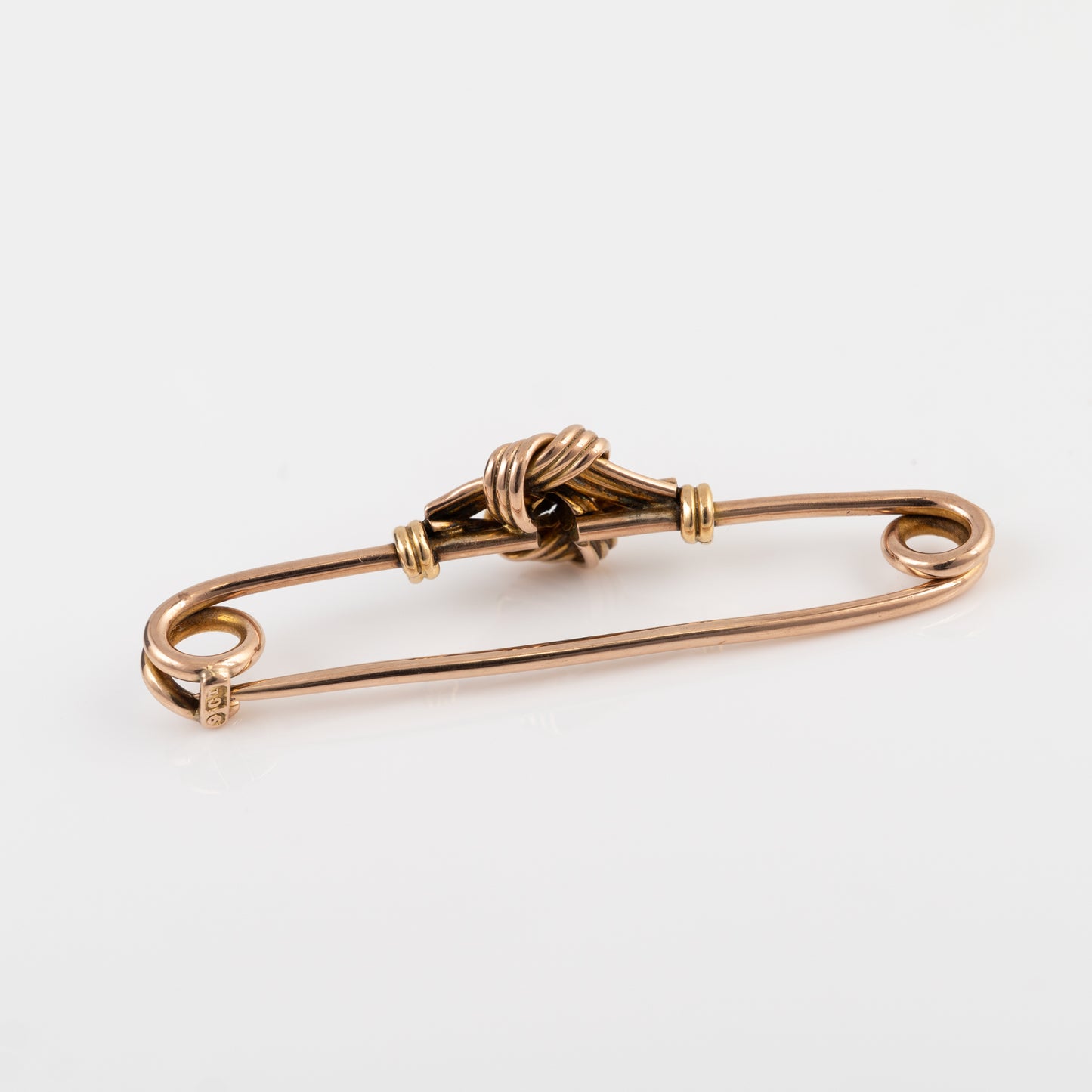 A gold brooch pin with a knotted decorative centre, photographed on a clean white background.