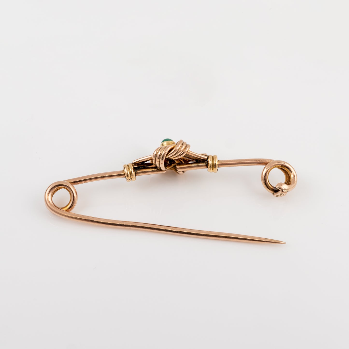 A vintage gold safety pin brooch with a small green stone accent at the center, displayed on a clean white background.