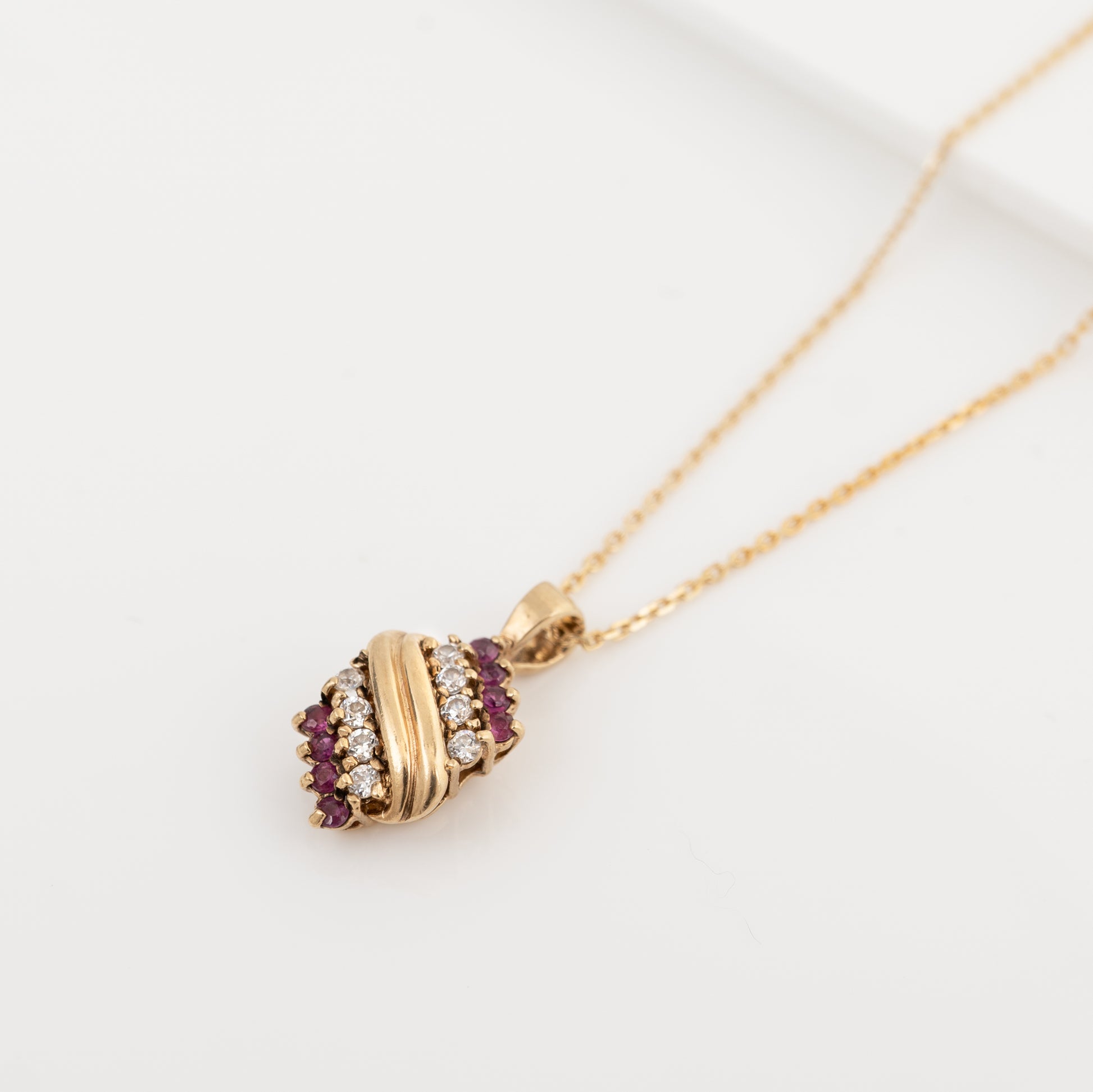 A gold pendant necklace featuring a wrap-style design with a central gold bar, flanked by rows of small clear stones and deep red gemstones, displayed on a clean white background.