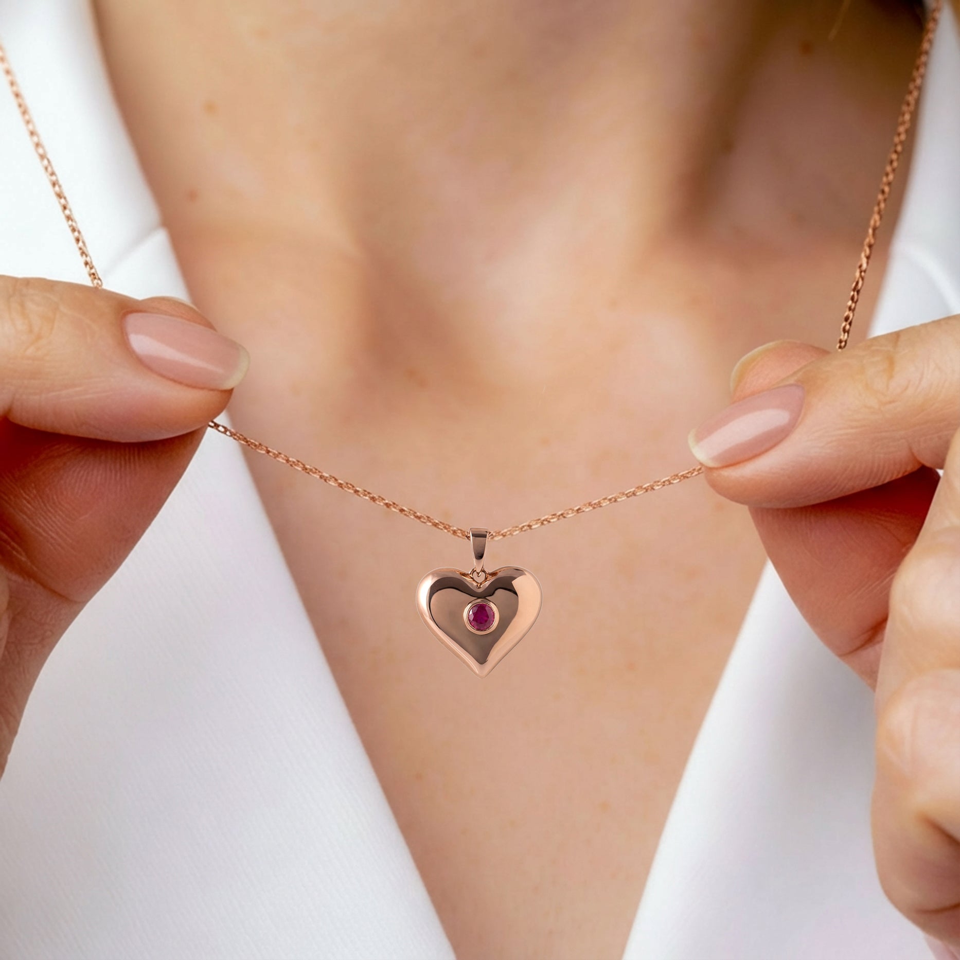 Rose gold heart-shaped necklace with a red gemstone on a person's neck.