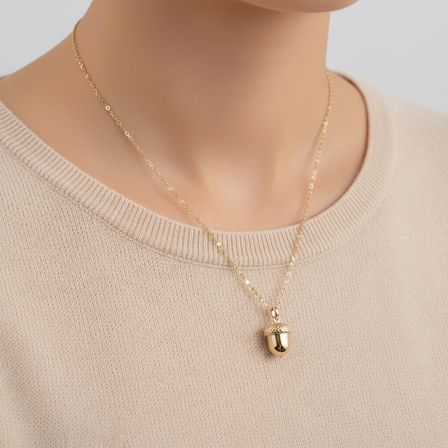Gold necklace with a pendant on a person wearing a beige sweater.