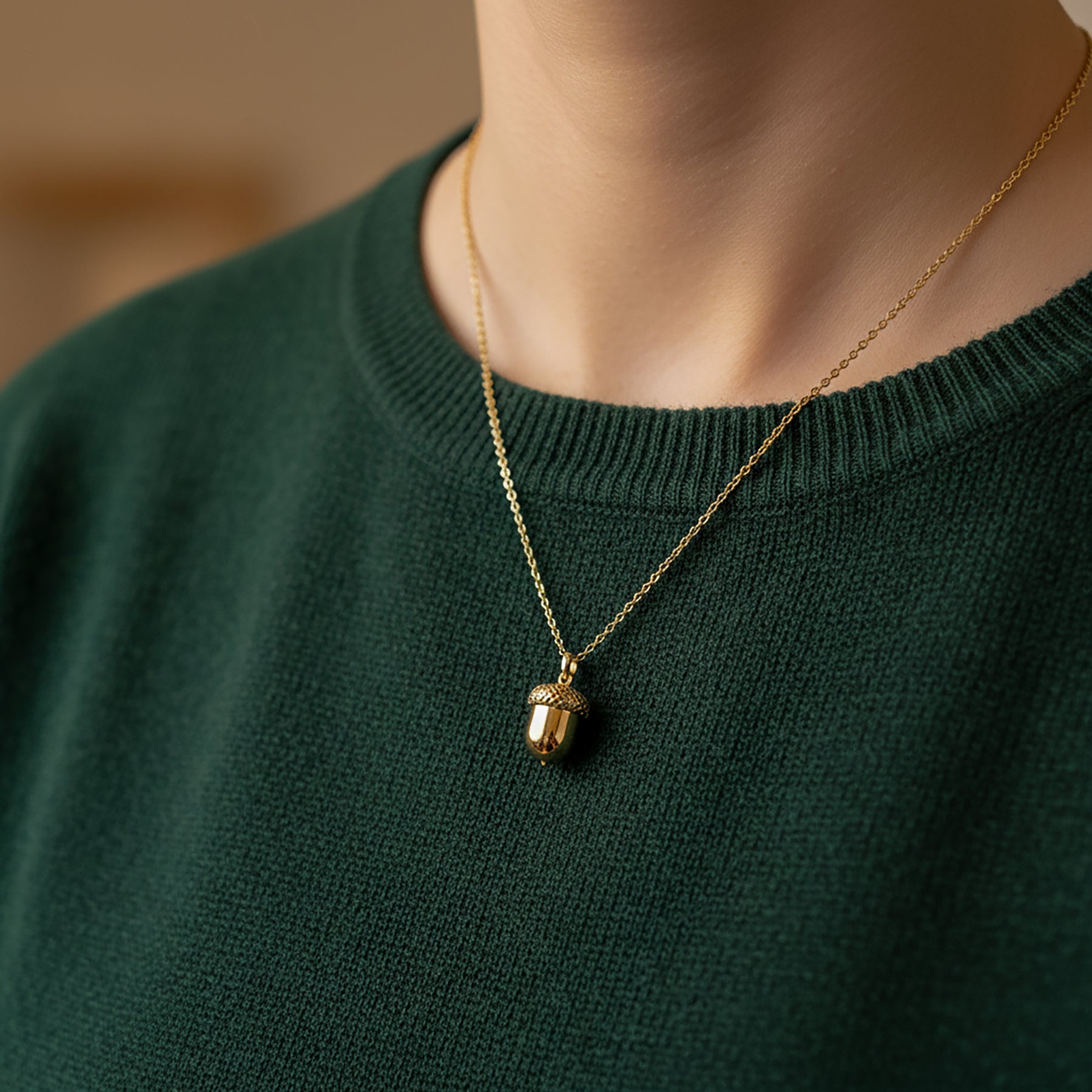 woman wearing dark green jumper with yellow gold acorn pendant