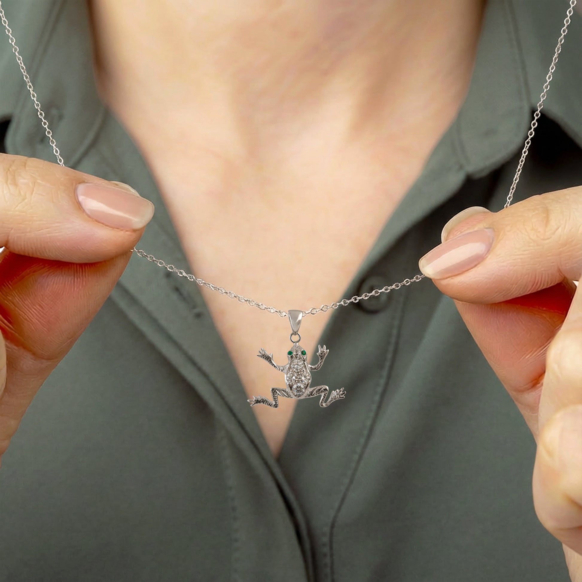 Person holding a silver necklace with a frog pendant against a neutral background