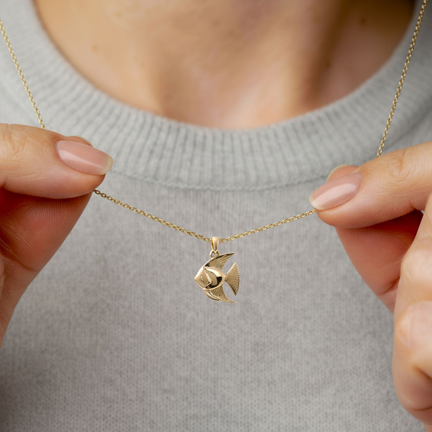Gold angelfish pendant necklace held by hands against a neutral background